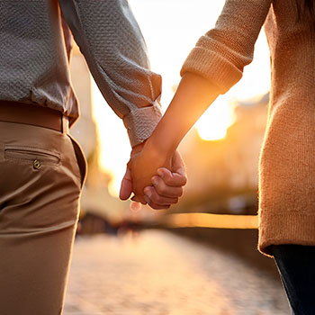 Couple holding hands while walking together at sunset