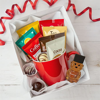Example of how to make a mug gift box. Pretty red mug with cocoa, tea, coffee packets, honey, and chocolates boxed in white tissue paper