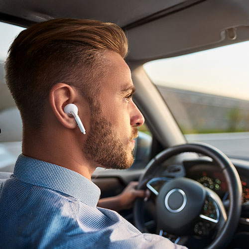 Man driving with wireless earbuds in, focused on the road